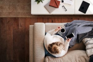 woman on couch looking at phone with coffee